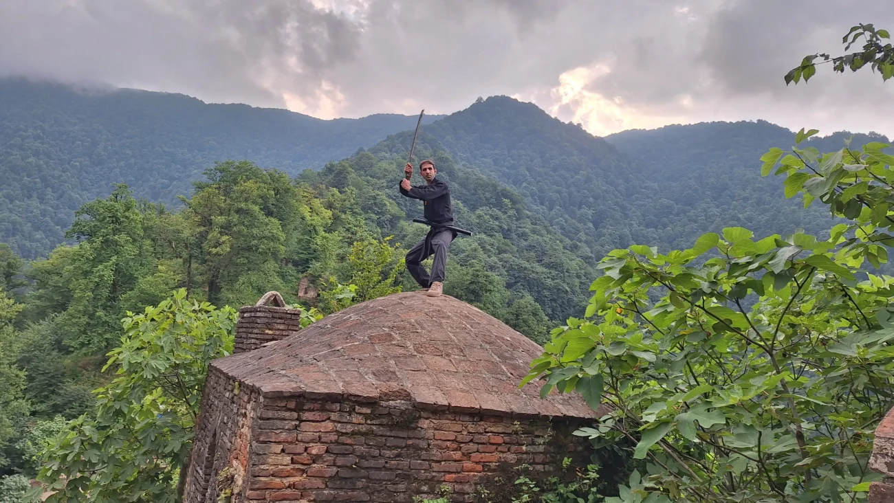 بنیانگذار بوجینکان لرستان در حال اجرای تکنیک نینجوتسو بر فراز سازه تاریخی در طبیعت سرسبز
